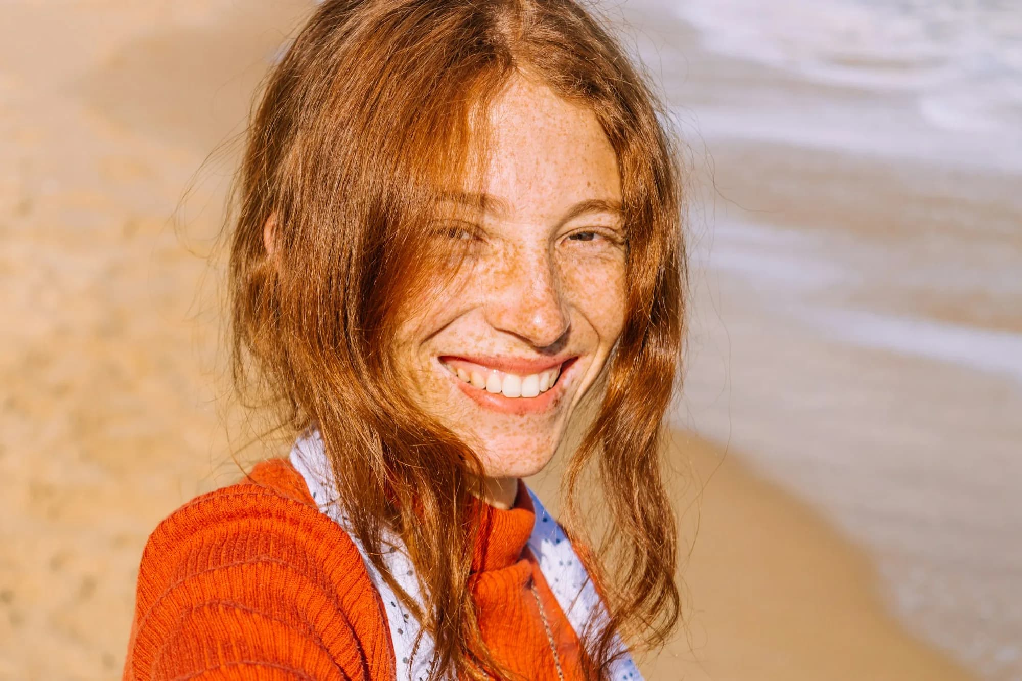 Happy young woman with red hair smiling on the beach