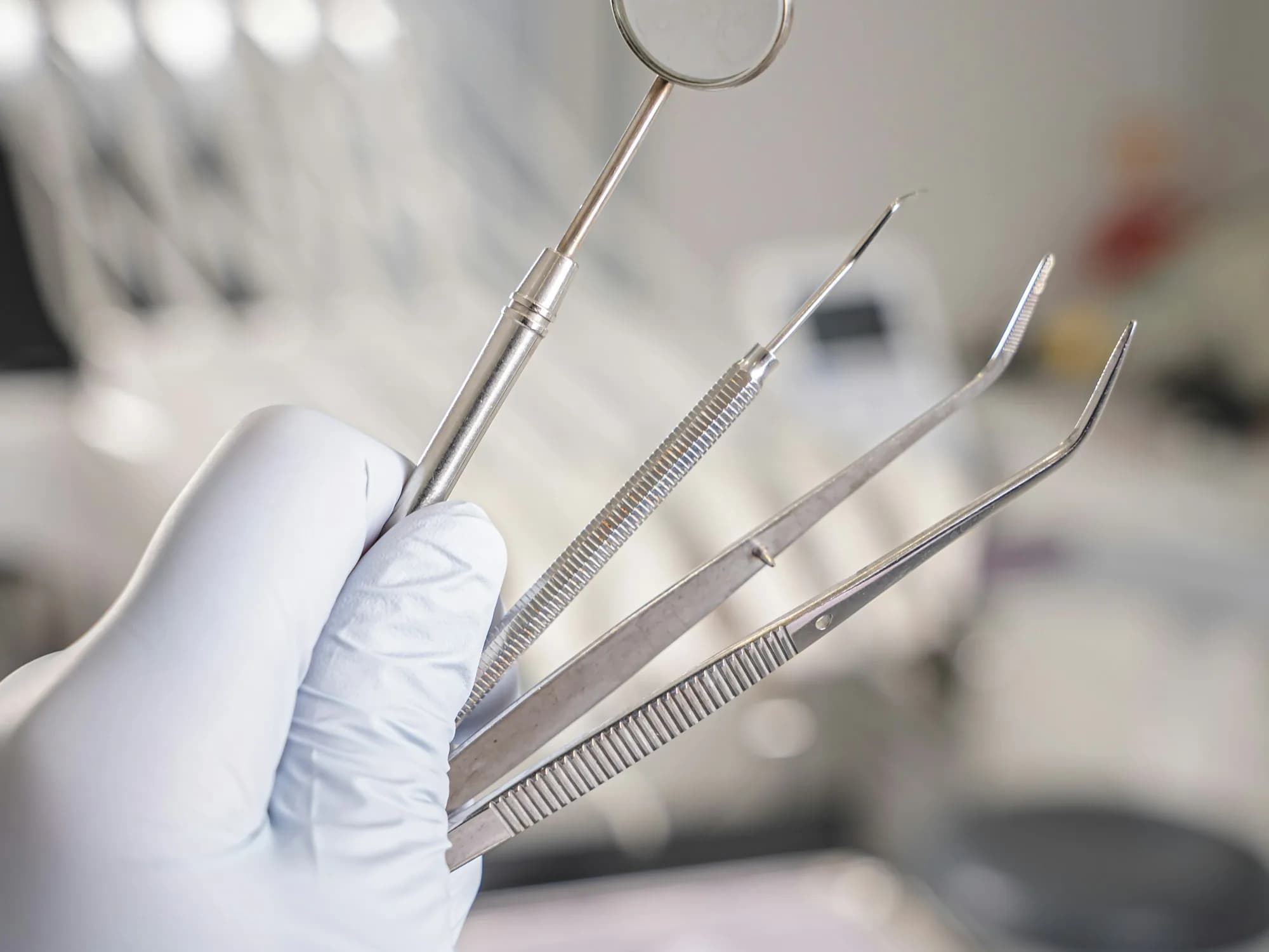 Gloved hand holding a dental mirror, probe and forceps